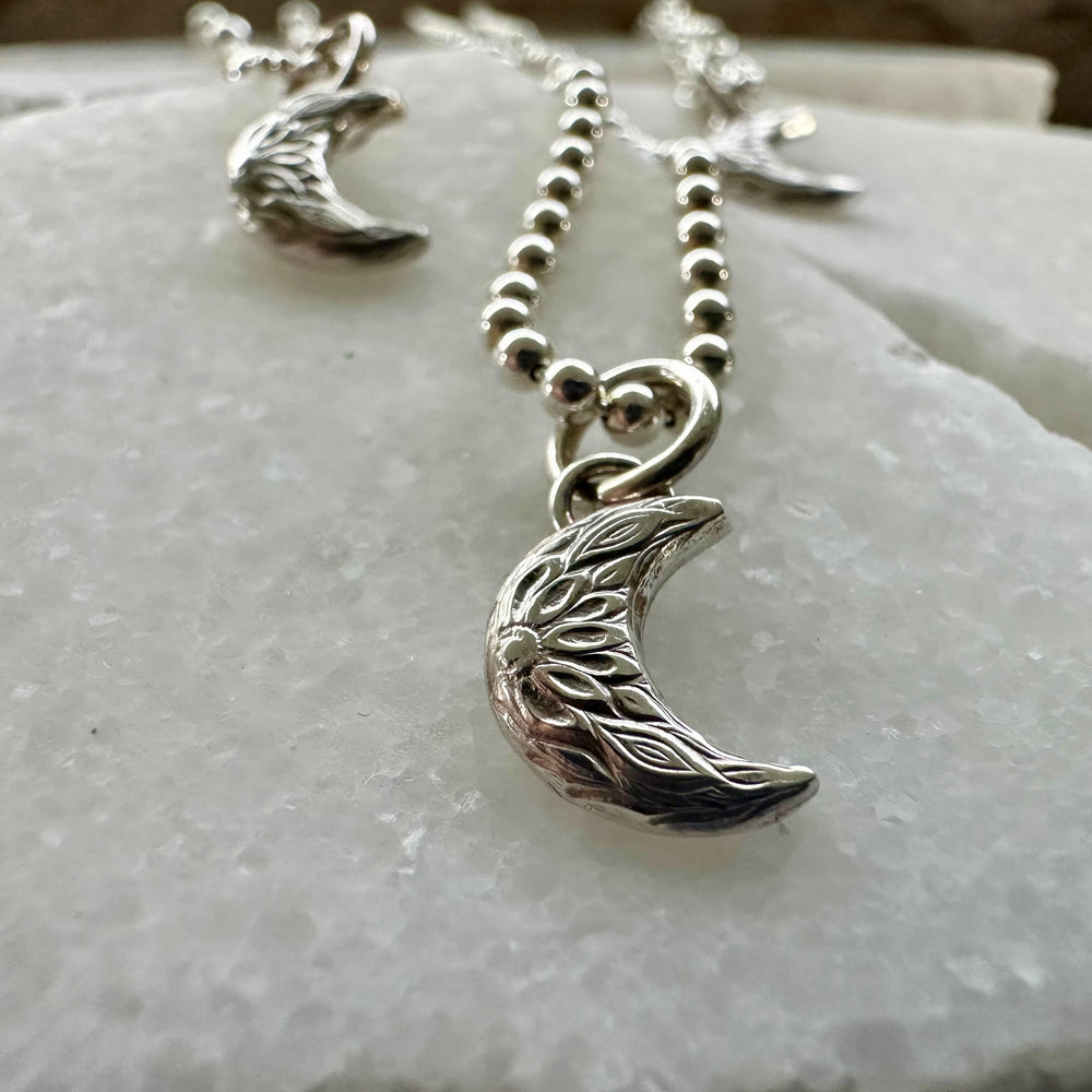 
                  
                    Handmade recycled silver crescent moon charm with rustic floral detail
                  
                